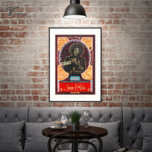 A framed  print of JIMI HENDRIX   hangs on a brick wall above a gray tufted sofa in a styled living room setting.