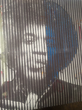 A close-up of a printed artwork or packaging featuring a stylized face formed by vertical white stripes over a dark background, with blue accents in the hair area.