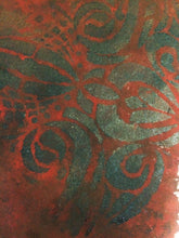 A close-up of a textured surface featuring an abstract, swirling pattern in dark green and burnt red.