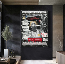 A large framed wall art print featuring a stylized portrait of hip-hop figure Nipsey Hussle with text and graffiti-style graphics, displayed on a dark wall in a modern interior setting.